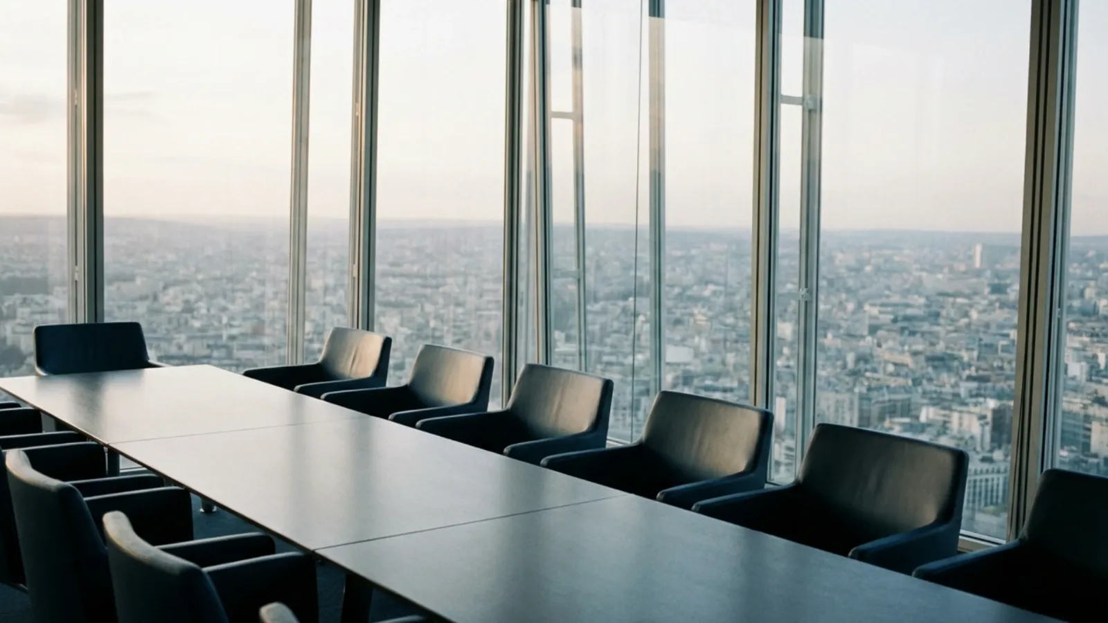 Salle de conseil vitrée en hauteur dans un quartier d’affaires, longue table vide en fin de journée