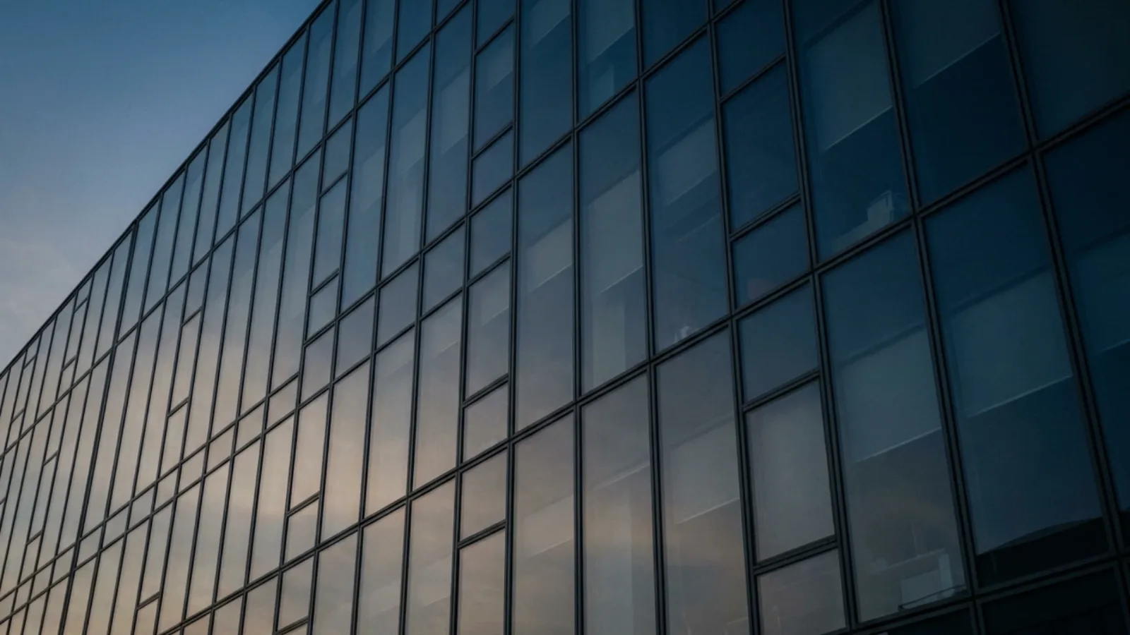 Façade vitrée d’un immeuble de bureaux vue en contre-plongée au crépuscule, les reflets du ciel dans les vitres