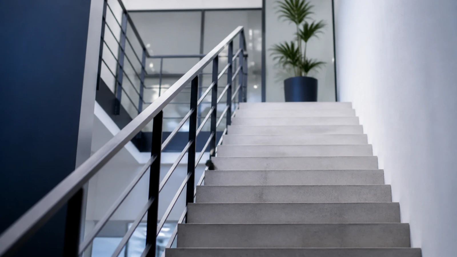 Escalier de béton clair d’un immeuble de bureaux vu en contre-plongée, rampe métallique